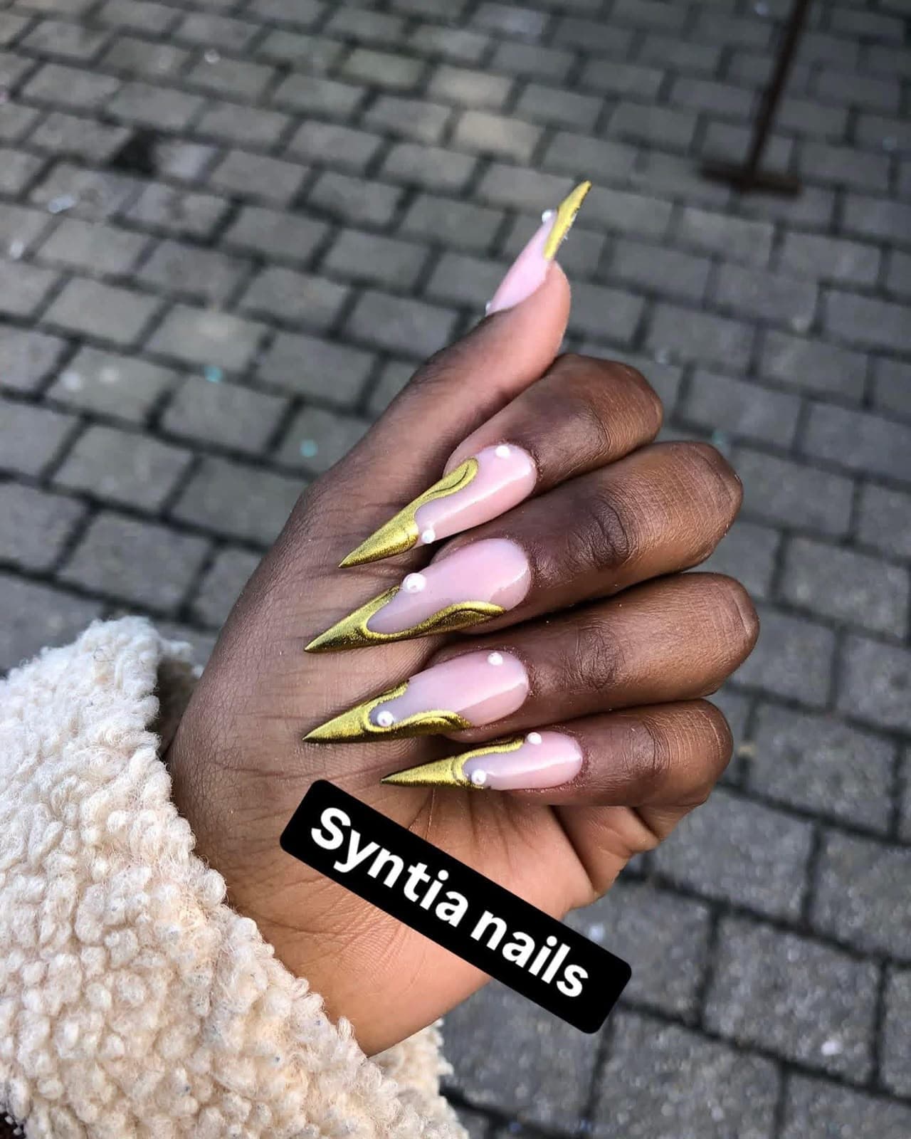 Stiletto nails with gold chrome wave tips and pearls on a pink nude base